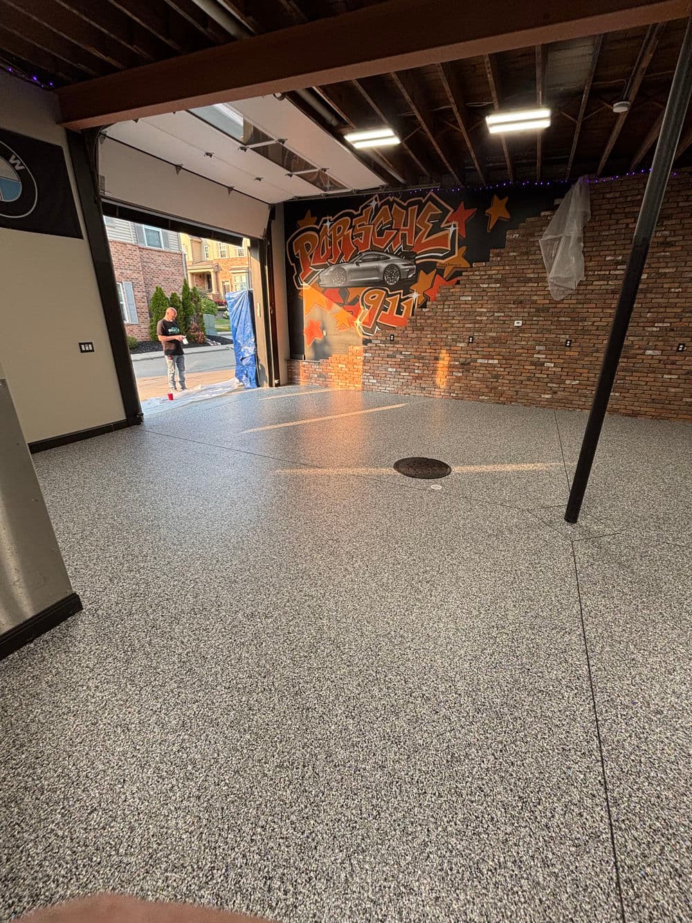 Garage interior with gray speckled flooring, Porsche 911 mural, and open garage door.