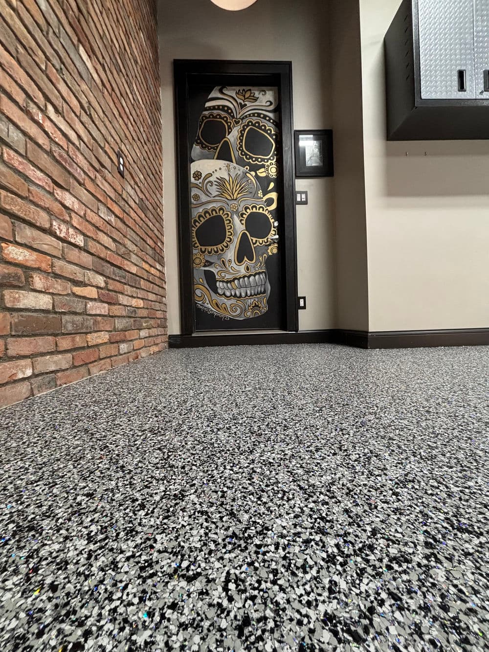 Decorative skull door design in a modern room with textured gray flooring and exposed brick wall.
